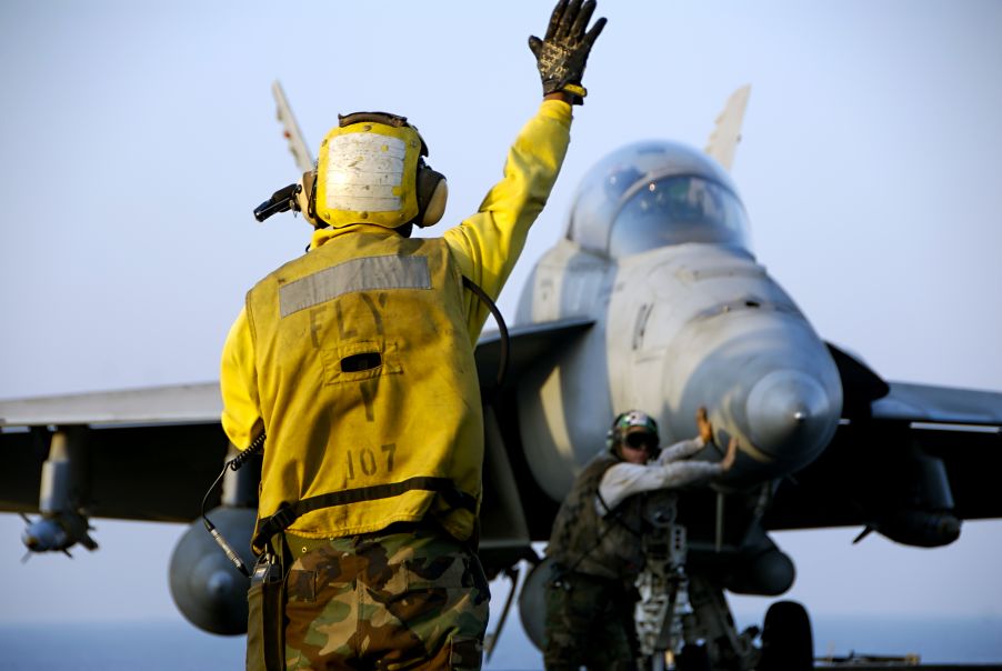 Ein Fluglotse dirigiert ein F-18 Hornet Kampfflugzeug über das Flugdeck eines Flugzeugträgers