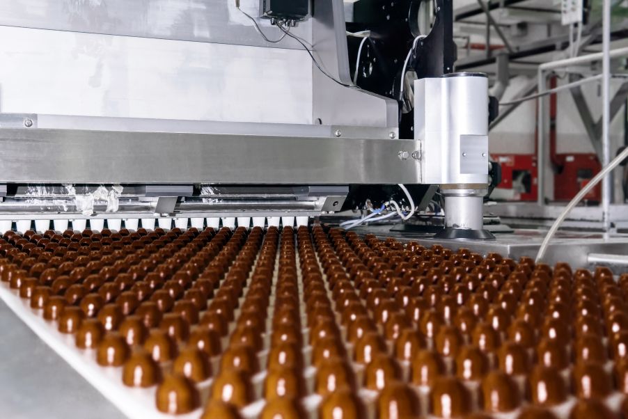 Filas de adición de cobertura para chocolates fabricados a máquina en una cinta transportadora (fábrica de chocolate)