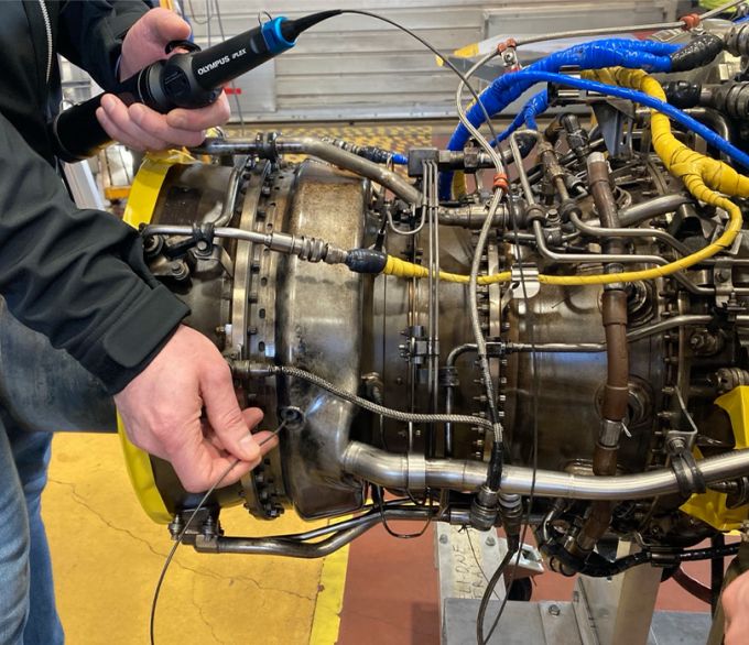 Inspector’s hands holding the IPLEX TX II borescope in one hand and guiding the insertion tube into an access  point in a GE CT7 turbine engine for a helicopter